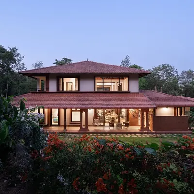 The Dream Coffee Estate in Coorg, seen at dusk. The home glows from within, its warm terracotta roof and laterite walls blending with the surrounding forest, creating a beacon of warmth and shelter.