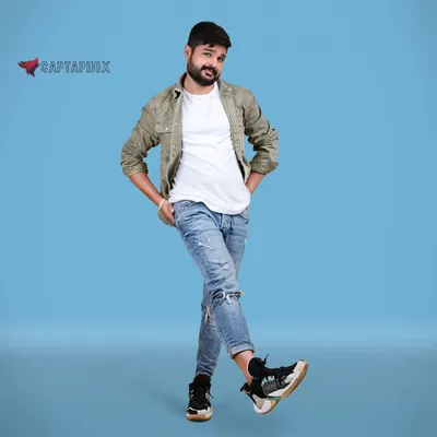 A full-length shot for a male model's portfolio, showcasing a casual, layered look. The solid blue backdrop provides a vibrant, clean setting that makes the subject and his relaxed pose the central focus.