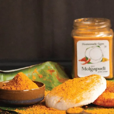 A classic South Indian breakfast scene featuring our authentic Molgapudi. This ground spice powder, served on a traditional banana leaf, is perfect for sprinkling over fluffy idlis, adding a burst of flavour and texture.