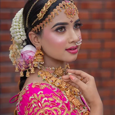 A close-up of a classic South Indian engagement look. The HD makeup provides a perfect canvas for the intricate temple jewellery, traditional matha patti, and a beautiful jasmine and rose braid.
