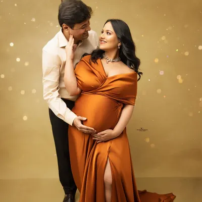 A glowing couple's portrait with a touch of magic. The mother-to-be looks radiant in a flowing rust-colored gown, complemented by sparkling light effects for a glamorous feel.