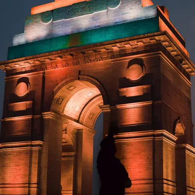India Gate stands majestically, lit in the colors of the Indian flag, with the silhouette of the Amar Jawan Jyoti statue. This is a powerful, atmospheric shot that captures a sense of national pride.