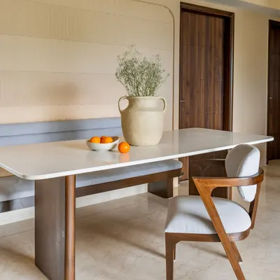 A modern dining nook from 'Project Lily,' featuring a sleek white-top table, a custom-built grey upholstered bench, and a stylish wooden dining chair. The textured wall adds warmth and depth.