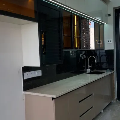A modern kitchen featuring a mix of beige and white high-gloss cabinets, a black granite backsplash, and tinted glass upper units with profile lighting.