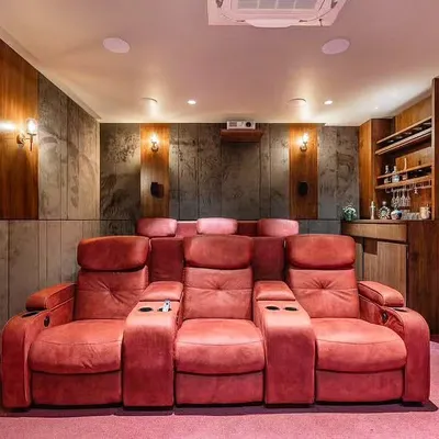 This is a dedicated home theater we designed for a client. It features plush, red recliner seating with cup holders, acoustic wall paneling, and a custom-built bar area at the back for a complete cinema experience.