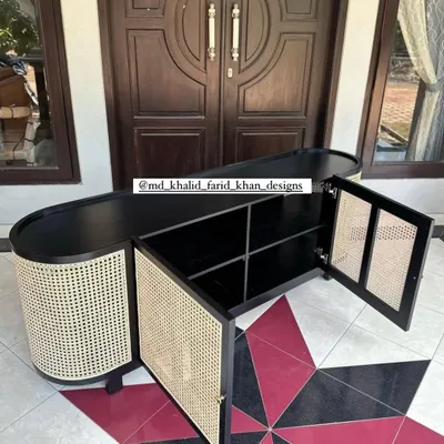 This custom-made sideboard features a unique oval shape with a black finish and cane-panelled doors. The doors are open to show the ample shelving inside, providing a stylish and practical storage solution for any entryway or dining room.