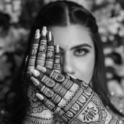 A black and white close-up that highlights the bold contrasts and intricate details of the henna. The lotus motif on the back of the hand is particularly striking in monochrome.