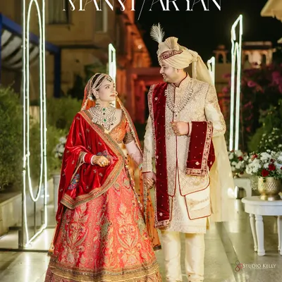 A royal couple portrait at night in Pushkar, with the groom in a classic sherwani and the bride in a traditional red lehenga, framed by the palace's illuminated archways.