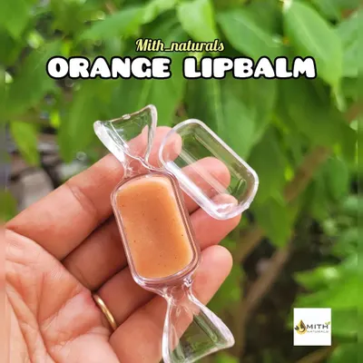 My homemade orange lip balm, shown here in its cute candy-shaped container. It's made to hydrate, heal chapped lips, and leave them feeling soft and moisturized.