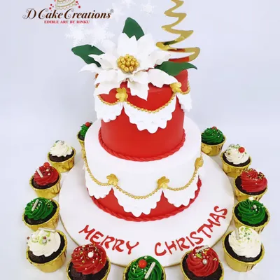 A festive two-tier Christmas cake, perfect for a holiday party centerpiece. This elegant creation features a red and white design with gold accents, a handmade sugar poinsettia, and is surrounded by matching red and green cupcakes.