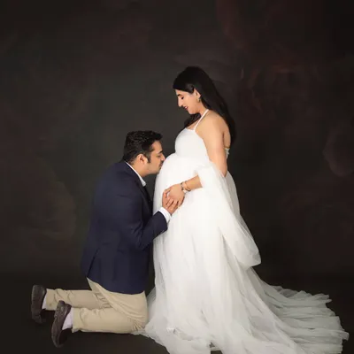A classic and heartfelt pose. The dad-to-be kneels to kiss the baby bump, showing so much love and anticipation. The mom-to-be looks ethereal in a flowing white tulle gown.
