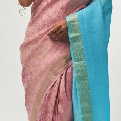 A detailed view of the silk linen fabric from the Aadya collection, showing the unique patina effect and the fine texture of the weave. The pink body contrasts beautifully with the blue pallu.