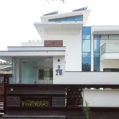 The contemporary exterior of Villa 9/21B, a private residence in Faridabad. The design is defined by its strong geometric lines, expansive glass panels, and a crisp white finish, creating a bold statement in modern residential architecture.