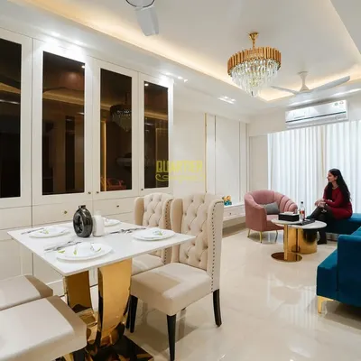 In this Tata Lavida, Gurugram home, I combined the living and dining areas into one cohesive, luxurious space. The design features a stunning crystal chandelier, plush tufted dining chairs, and a rich blue sofa, all tied together with elegant white and gold-accented cabinetry.
