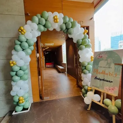 A lovely balloon arch in sage green and white for a baby shower entrance, complemented by a personalized welcome sign on an easel.
