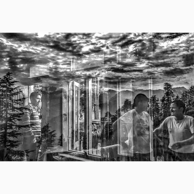 An in-camera reflection from Jibhi, Himachal Pradesh, blending the interior scene of people talking with the dramatic clouds and mountains outside. This black and white conceptual piece merges human interaction with the power of nature.