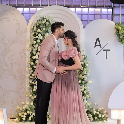 A beautiful moment captured at an elegant baby shower. The parents-to-be pose in front of a modern backdrop of white arches and cascading white roses, perfectly showcasing the event's chic and serene theme.