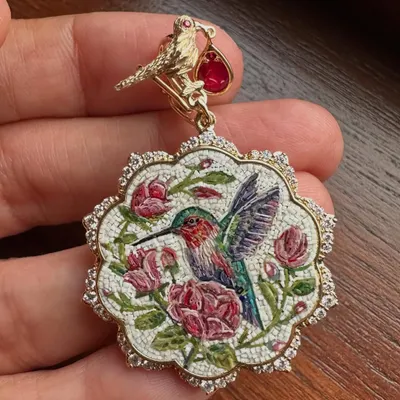 A close up of the hummingbird and roses pendant. You can see the individual tiles that form the image, a testament to the patient and detailed process of micromosaic art, all set with natural diamonds and a Mozambique ruby.