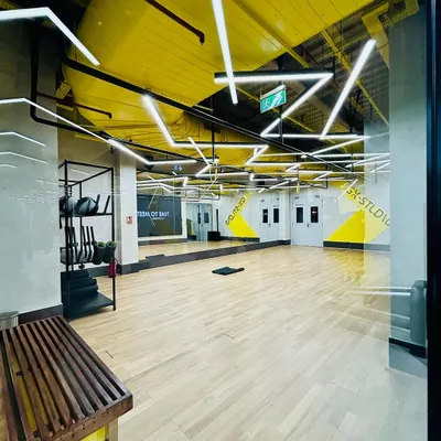The group exercise studio at DLF Thrive in Chennai. The design features high-contrast yellow geometric patterns and dynamic overhead lighting on a wood-finish floor, creating a vibrant and motivating space for classes.