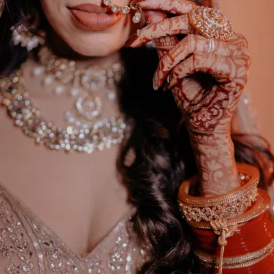 A close-up on the bride's hands, showcasing her beautiful bridal choora, intricate mehndi, and elegant nath. These details tell a story.
