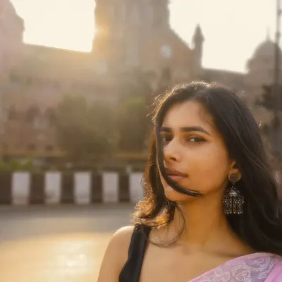 A classic Mumbai street portrait, with the iconic architecture softly backlit by the morning sun. The wind in her hair adds a perfect, candid touch.