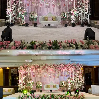 A dreamy pastel pink and white stage for a wedding reception. The cascading floral arch and delicate hanging details create a soft, romantic focal point for the couple.