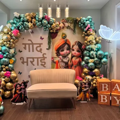 A beautiful 'Godh Bharai' ceremony with a Krishna theme. The decor features a backdrop of baby Krishna and Radha, surrounded by a teal and gold balloon arch and neon butterfly lights.