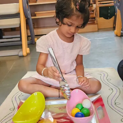 A child carefully transfers items with a large spoon, an activity that develops fine motor skills, concentration, and coordination. These practical life exercises are the foundation of the Montessori method, preparing children for life.