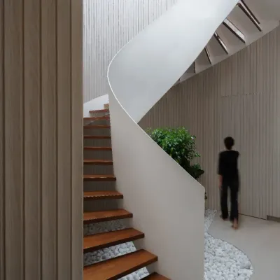 The helical staircase in the Hemadri penthouse is a central feature. Its swirling white form contrasts beautifully with the warm wood treads and the linear fluted wall, creating a dynamic yet elegant focal point.