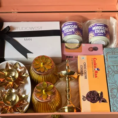 A premium gift hamper for a man, featuring grooming products from Studio West, Moroccan Escape candles, and gourmet cookies. The elegant pink trunk and traditional brass lamp make it a sophisticated gift.