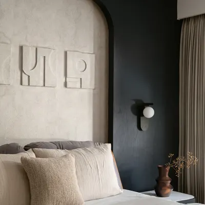 In this bedroom, I explored the power of a monochrome palette to create a space that is both youthful and sophisticated. The design is built on layers of texture, from the lime-washed wall behind the bed to the abstract art and soft linens. Every detail, including the modern wall sconce and custom headboard, was chosen to make the compact room feel intentional and full of character.