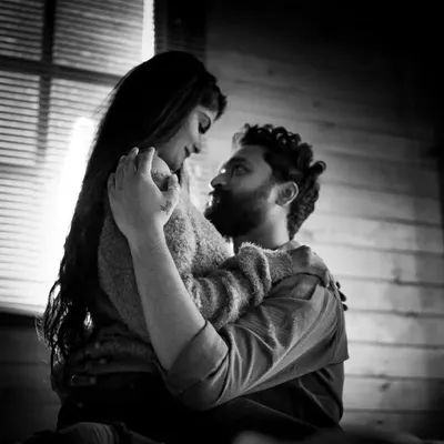 An intimate black and white portrait of a couple embracing. The dramatic lighting and their close connection create a powerful and emotional image that feels both timeless and deeply personal.