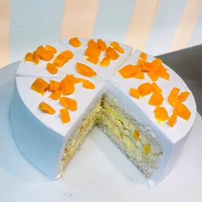 A slice taken from our fresh Mango Cake, revealing layers of light sponge and fresh mango pieces inside. A true taste of summer.