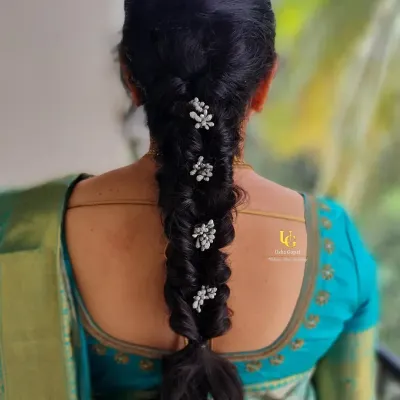 A classic and elegant hairstyle for a traditional event. This is a neatly twisted braid adorned with delicate, pearl-like floral accessories, perfect for a silk saree look.