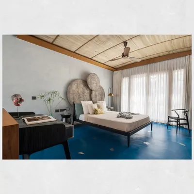 The master suite in the Kamala Residence is a study in texture. A ceiling of locally sourced banana fiber mats, blue oxide flooring, and a headboard made of distressed wood panels create a tropical, earthy ambiance.