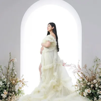 A beautiful silhouette of an expectant mother in a cream-colored ruffled gown. The bright light from the arched window behind her creates a heavenly, glowing effect.