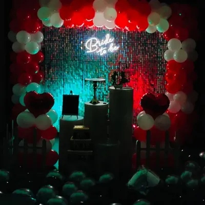 A "Bride to be" party setup seen in low light, where the neon sign and red accents truly pop. The dramatic lighting against the shimmer wall creates a chic and exciting atmosphere for the celebration.