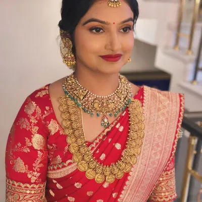 A close-up of Dr. Nayana's classic South Indian makeup look. The bright red lip and defined eyes pair perfectly with her traditional gold temple jewelry and red silk saree.