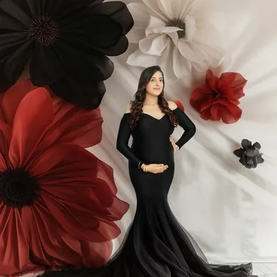 A portrait that feels like a piece of art. The expecting mother is framed by giant paper flowers, wearing an elegant black mermaid gown that beautifully highlights her form. This is a classic, dramatic maternity look.