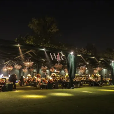 A spectacular wide view of an outdoor reception we designed. The entire space is enveloped in emerald green draping, with dozens of chandeliers creating a ceiling of light, transforming a simple lawn into a luxurious, otherworldly ballroom.