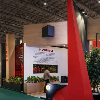 The entrance to the Virgo exhibition stall is marked by a dramatic, tapering red form that funnels visitors into the space. This bold geometric element acts as a powerful landmark within the busy exhibition hall.