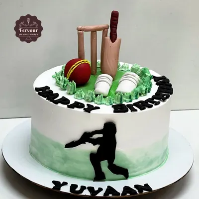 A classic cricket theme cake for a true fan. This design features a fondant bat, ball, and wickets on a field of green whipped cream, with a silhouette of a batsman on the side.