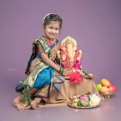 A lovely portrait of a young girl dressed in a traditional Paithani saree for a Ganpati photoshoot. She sits beside a Ganpati idol with a beautiful smile, creating a perfect festive memory.