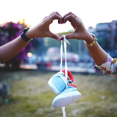 A classic and creative pregnancy announcement photo. The parents-to-be form a heart with their hands, holding a tiny pair of baby shoes, symbolizing their love and anticipation.