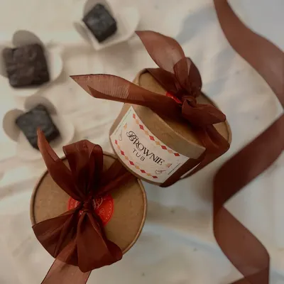 Introducing our brownie tubs! A fudgy, eggless brownie drenched in rich chocolate sauce, elegantly packaged in a round tub with a ribbon. One spoonful and you’re hooked.