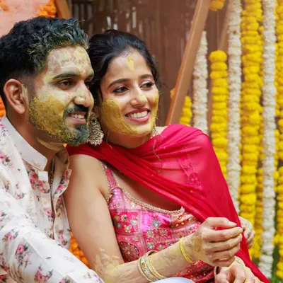 A candid moment from a Haldi ceremony, full of smiles and laughter. The backdrop of traditional marigold garlands adds a burst of auspicious yellow, perfectly capturing the spirit of the event.