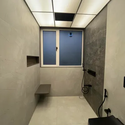 This modern bathroom in our Sanpada project features a stunning backlit stretch ceiling that provides even, diffused light. The floating bench and niche in the shower area add both style and practicality.