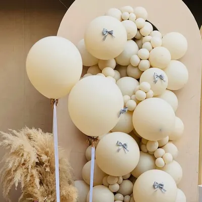A close-up of our 'Babies in Bloom' boho decor, showing the delicate silver bow details on the cream-colored balloons and a hint of pampas grass.