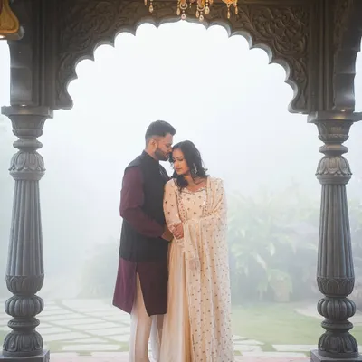 A couple shares a quiet moment under the grand archway, framed by the warm light of the chandelier. The mist in the background adds a layer of romance to this pre-wedding portrait.