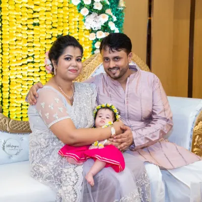A beautiful family portrait taken during an Annaprasan ceremony. The parents are dressed in traditional wear, holding their baby girl, all smiling together.